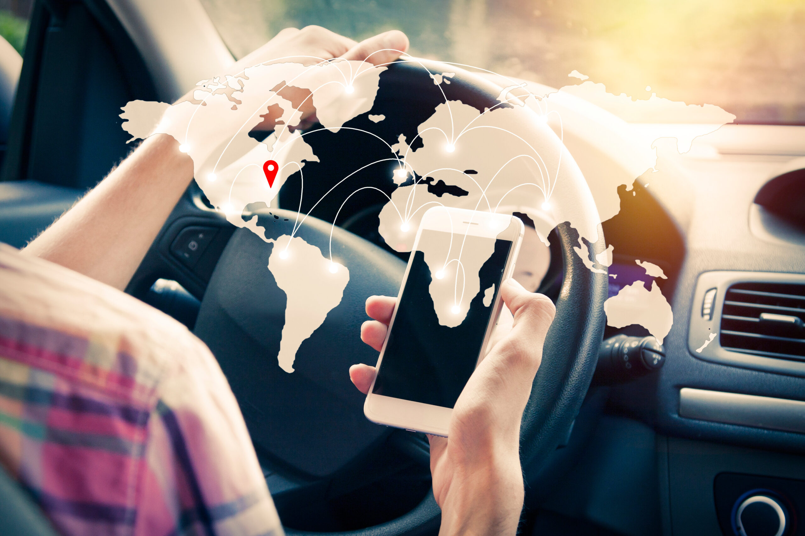 Person am Steuer hält ein Smartphone; darüber liegt eine Weltkarte mit vernetzten Standortpunkten, die globale Ortung und Geofencing symbolisieren.