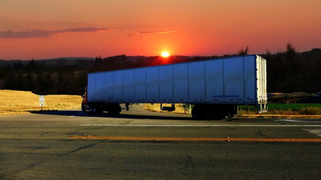 LKW fährt richtung Sonnenuntergang, seitlich fotografiert.